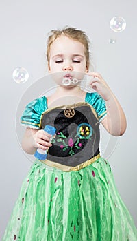 Beautiful little blonde girl, has happy fun cheerful smiling face, pink dress, soap bubble blower. Portrait with pink and white