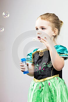 Beautiful little blonde girl, has happy fun cheerful smiling face, pink dress, soap bubble blower. Portrait with pink and white