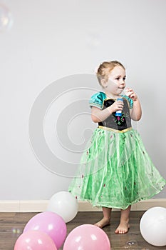 Beautiful little blonde girl, has happy fun cheerful smiling face, pink dress, soap bubble blower. Portrait with pink and white