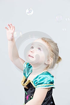 Beautiful little blonde girl, has happy fun cheerful smiling face, pink dress, soap bubble blower. Portrait with pink and white