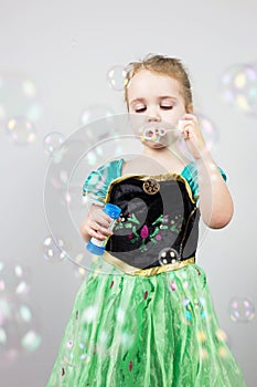 Beautiful little blonde girl, has happy fun cheerful smiling face, pink dress, soap bubble blower. Portrait with pink and white