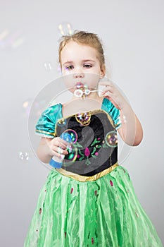 Beautiful little blonde girl, has happy fun cheerful smiling face, pink dress, soap bubble blower. Portrait with pink and white