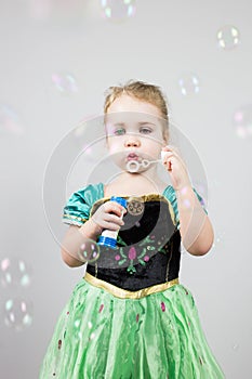 Beautiful little blonde girl, has happy fun cheerful smiling face, pink dress, soap bubble blower. Portrait with pink and white