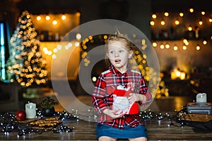 A beautiful little blonde girl received a sweet Christmas gift sitting on a wooden table in a decorated house