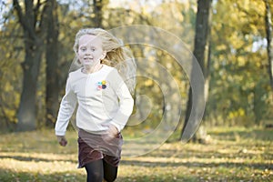Beautiful little blonde girl runs in an autumn park.