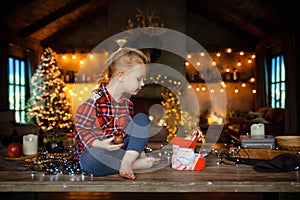 A beautiful little blonde in a traditional plaid shirt opens a chocolate bar from her sweet Christmas gift