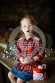 A beautiful little blonde girl received a sweet Christmas gift sitting on a wooden table in a decorated house