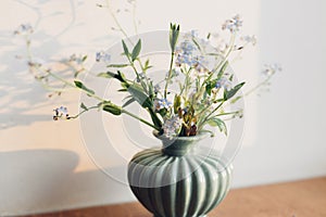 Beautiful little blue flowers in vase in warm sunlight on rustic wooden background. Delicate myosotis petals, forget me not spring