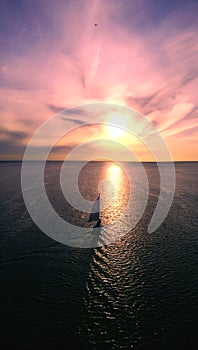 Beautiful little boat floats toward the horizon on the background of the sunset coloured sky. The view from the air.