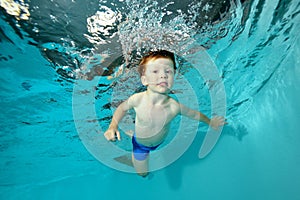 Beautiful little boy swimming underwater in pool on blue background. Portrait. Shooting under water at the bottom.