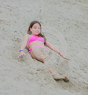 Beautiful little brunette girl in pink bathing suit sitting in the sand