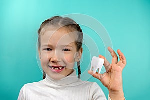 Beautiful little Caucasian girl holding little model of tooth on a blue background