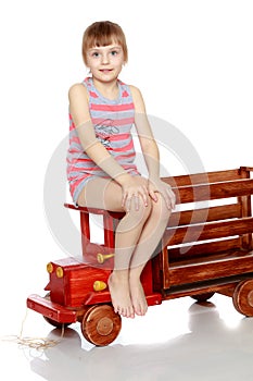 The girl is sitting on a large toy wooden car.