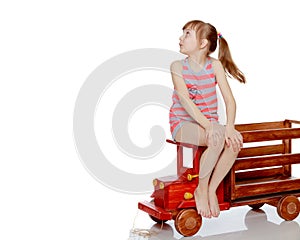 The girl is sitting on a large toy wooden car.