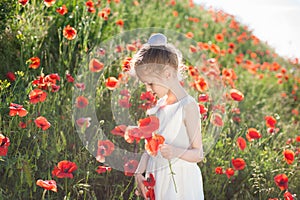 Beautiful little caucasian girl in white dress holding poppy red in green summer field