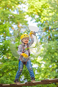 Beautiful little child climbing and having fun in adventure Park. Hiking in the rope park girl in safety equipment.