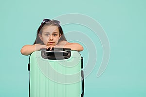 Beautiful little child girl looking at camera, posing with blue suitcase, isolated over studio background. Copy ad space