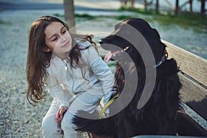 Beautiful little child girl talking to her best companion - a black young cocker spaniel dog, sitting together on the