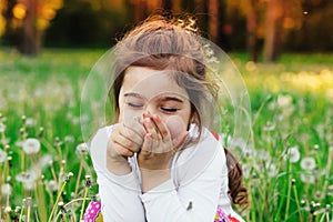 Beautiful little child smiling with dandelion flower in sunny summer park. Happy cute kid having fun outdoors at sunset.