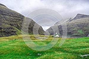 Beautiful little church, with a grassy roof, against the backdrop of beautiful mountains, and dramatic clouds. Faroe