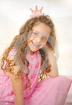 Beautiful little curly girl posing for camera and wearing a pink princess dress