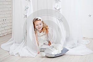 Beautiful little curly-haired girl in a white dress, shot in bright studio decorations