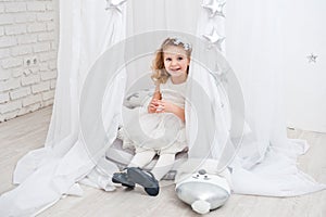 Beautiful little curly-haired girl in a white dress, shot in bright studio decorations