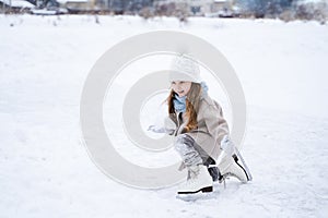 Beautiful little cute girl learn to skate on ice skating rink in park. Fall down and have fun. Stylish look, warm woolen coat,