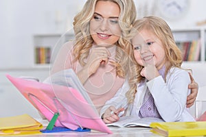 Beautiful little cute girl reading book with mother at the table at home