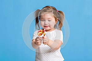 Beautiful little female child holding huge lollipop spiral candy smiling happy isolated on blue background.