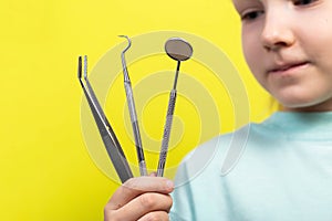 A beautiful little girl aged seven years old holds dental instruments on a yellow background. The concept of treatment