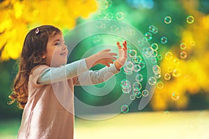 Beautiful little girl playing with yellow leaves and soap bubbles in a autumn park