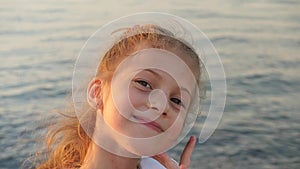Beautiful little girl on a background of sea sunset smiles showing teeth