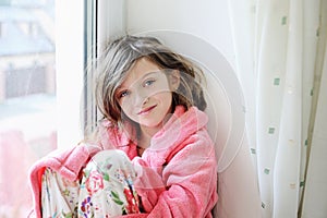 Beautiful little girl in bathrobe near window