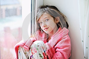 Beautiful little girl in bathrobe near window