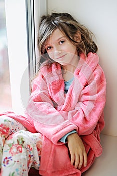 Beautiful little girl in bathrobe near window