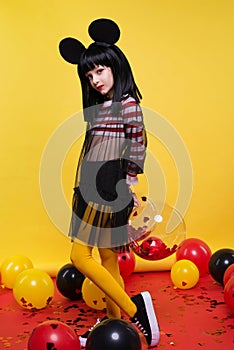 Beautiful little girl in black wig posing over bright yellow background