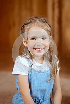 Beautiful little girl blonde curly hair, bright emotions, gentle image. Girl posing on beige background in blue dress, little