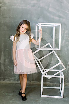 Beautiful little girl with broun long hair on a grey background near the white constructure of the cubes