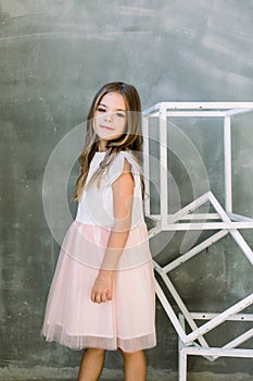 Beautiful little girl with broun long hair on a grey background near the white constructure of the cubes