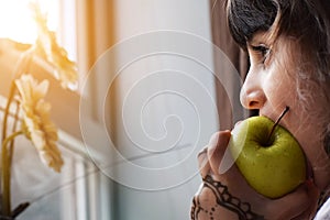 Beautiful little Girl child kid portrait eating green healthy Apple while looking outside from home window on sunny day