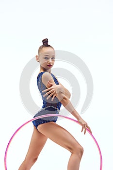 Beautiful little girl child, rhythmic gymnast in blue stage costume standing with hoop against white studio background