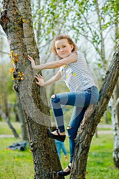 Beautiful little girl climbed tree. child in ripped jeans. Wild life of modern children. Outdoor adventure