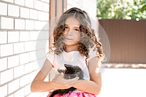 Beautiful little girl with curls holds a kitten in her arms