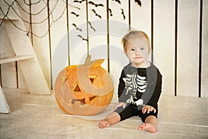 Beautiful little girl with Down syndrome sitting near a pumpkin on Halloween dressed as a skeleton