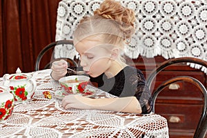 Beautiful little girl drinking tea at the table.