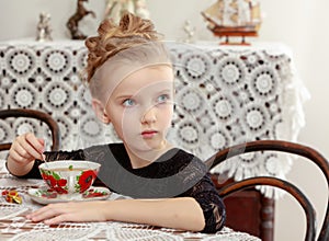 Beautiful little girl drinking tea at the table.