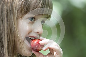 Beautiful little girl eating a juicy red strawberry