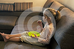 Beautiful little girl eating unhealthy food while watching TV at the sofa