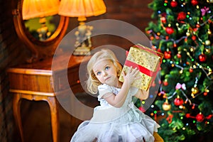 Beautiful little girl in a festive dress opens a gift